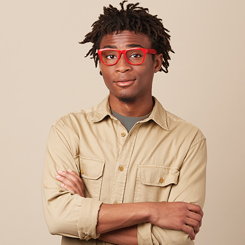 Person wearing red glasses and a beige button-up shirt with folded arms.