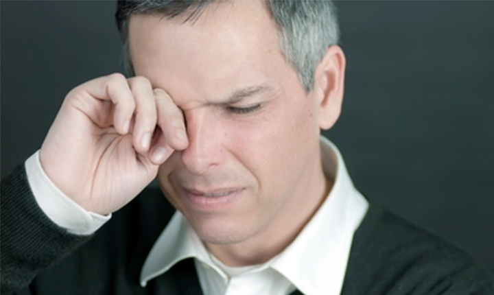 Man rubbing his eye as if in discomfort or pain.