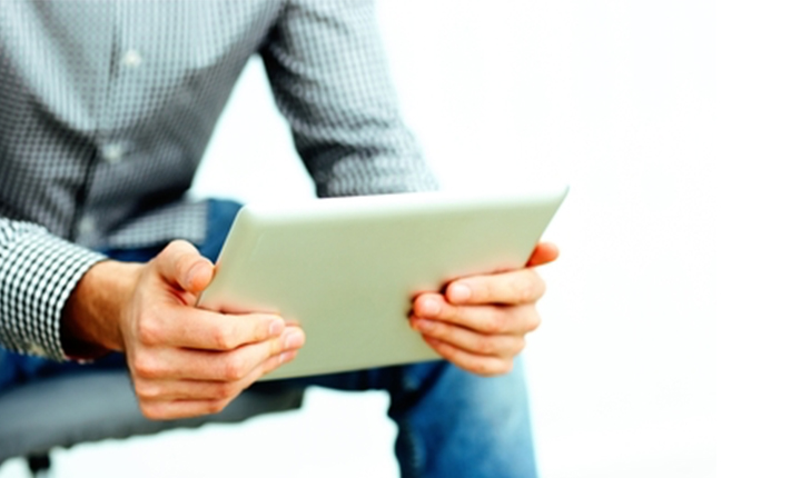 Person holding a tablet with both hands, sitting down, wearing a buttoned-up shirt and jeans.