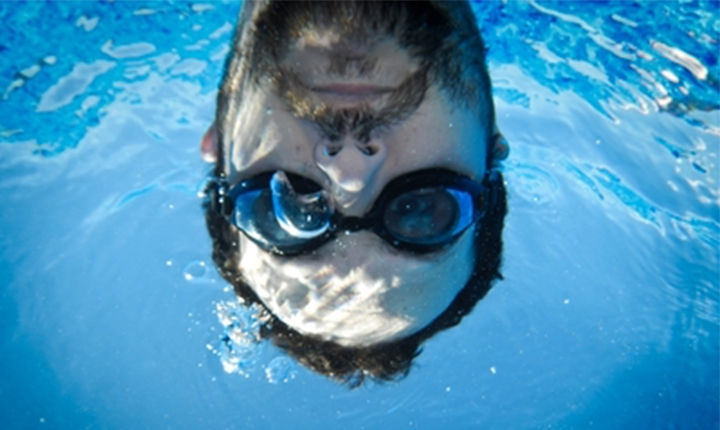 Man wearing swimming goggles underwater, face half submerged.