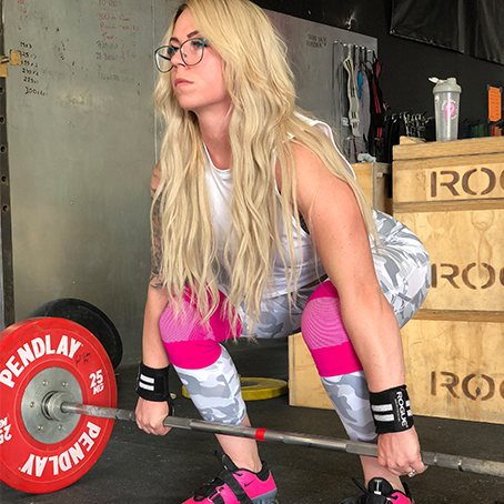 Woman lifting a Pendlay barbell with 25kg weights, wearing pink knee sleeves and pink weightlifting shoes.