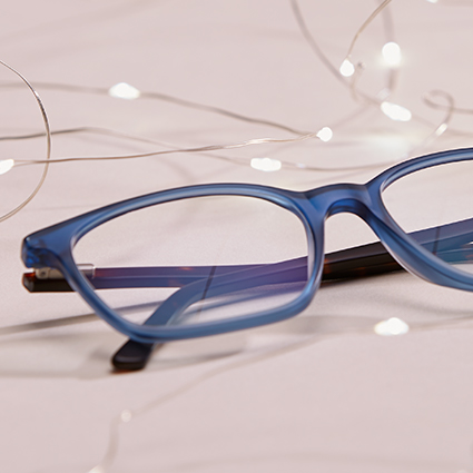 Blue prescription eyeglasses with rectangular frames placed on a white surface, with fairy lights in the background.