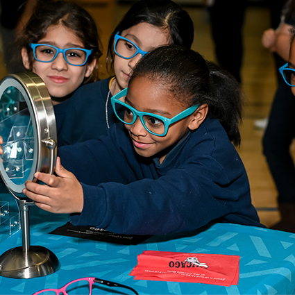 Children trying on turquoise-framed glasses in front of a mirror.