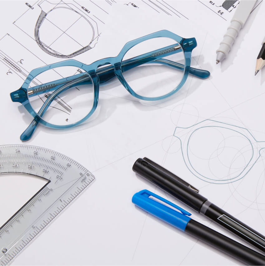 Blue Zenni eyeglasses sit on a drawing table with rulers, pens, and pencils.