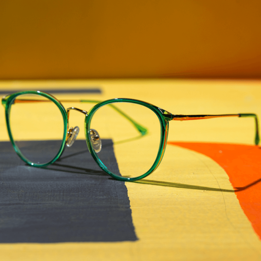 Green-rimmed eyeglasses with thin temples laying on a multicolored surface.