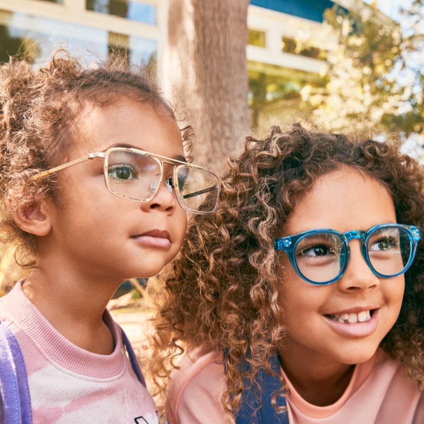 Two children wearing colorful eyeglasses; one with gold frames, the other with blue frames.