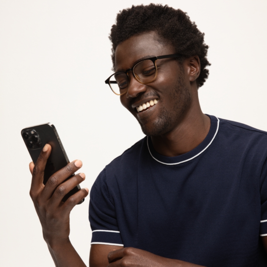 Man in glasses smiling while holding a black smartphone.