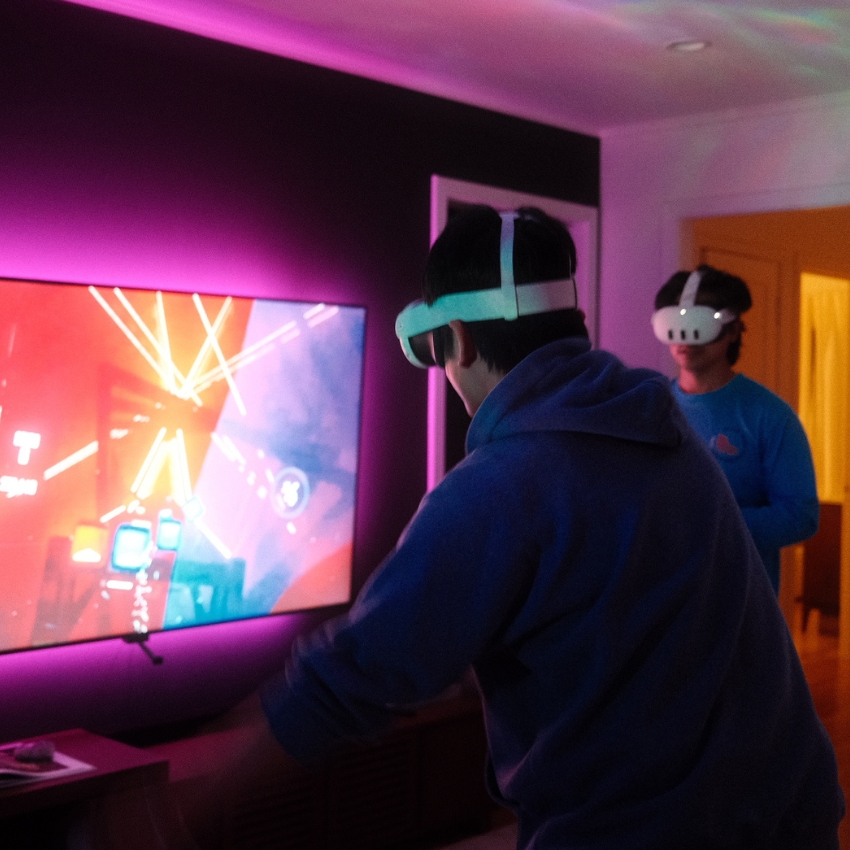 Two people playing a virtual reality game with headsets in front of a brightly lit screen.