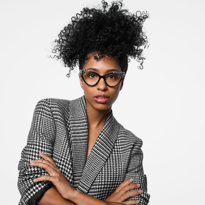 Woman wearing black and white houndstooth-patterned blazer and black eyeglass frames with spotted design.