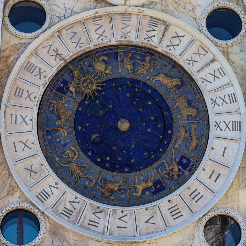 Astronomical clock with zodiac signs, Roman numerals, and a decorative sun in the center.