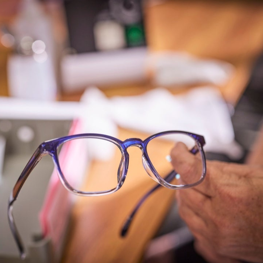 Hand holding modern blue gradient eyeglasses with rectangular lenses.