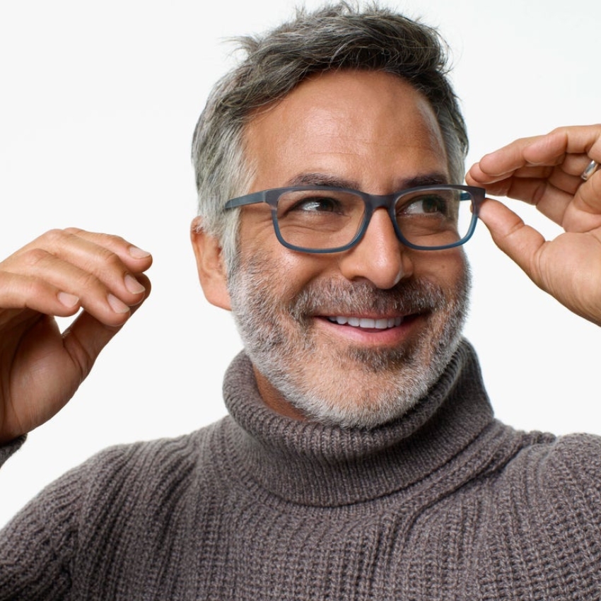 Man adjusting stylish grey eyeglasses while smiling and wearing a grey turtleneck sweater.