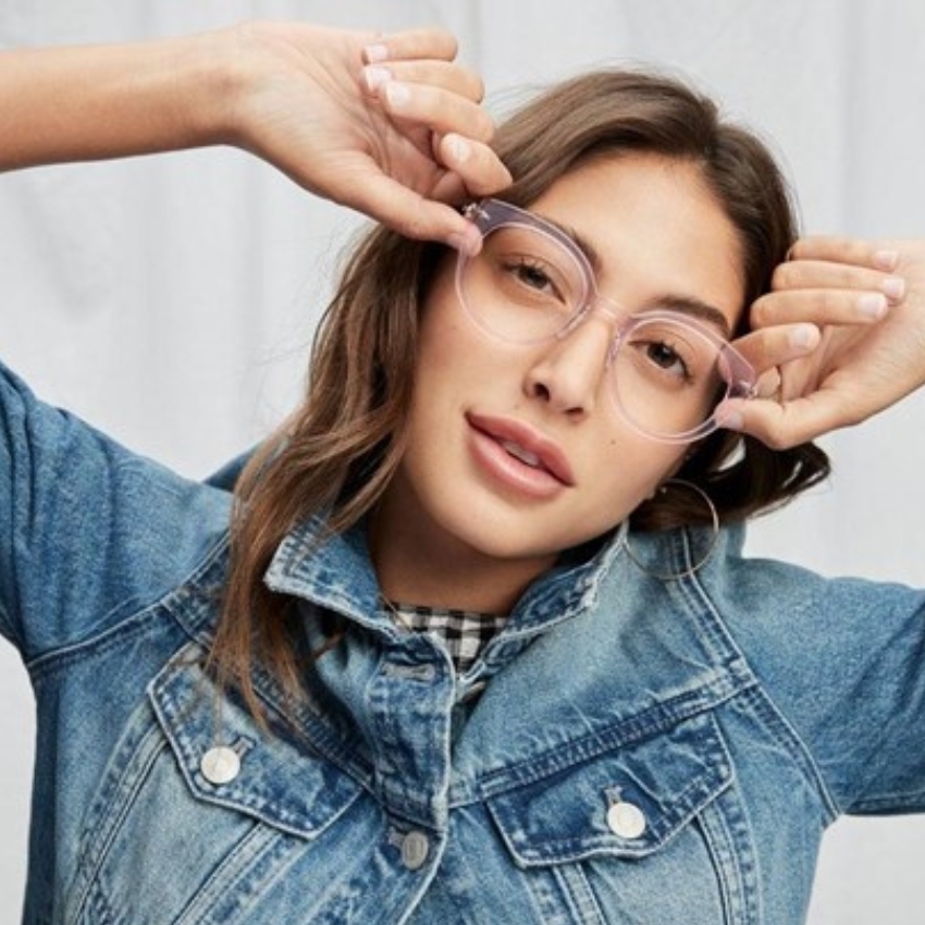 Woman wearing clear, round eyeglasses and a blue denim jacket.