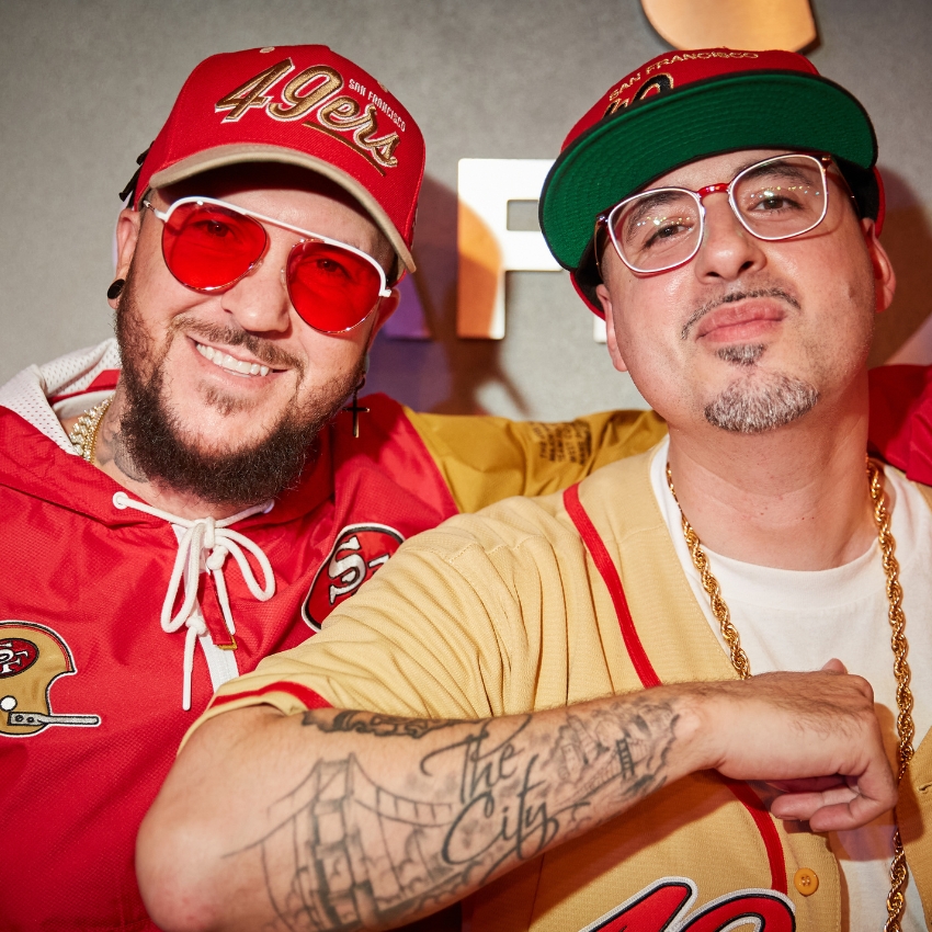 Two individuals wearing San Francisco 49ers hats, jerseys, and red-tinted glasses. One has a "The City" tattoo.