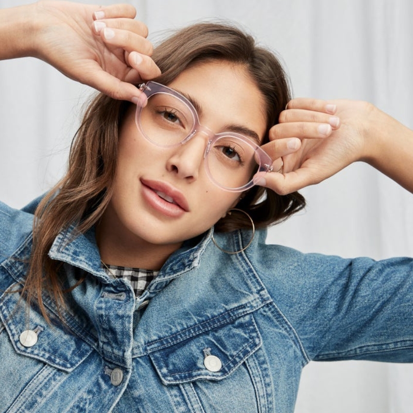 Woman wearing clear, round eyeglasses and a denim jacket.