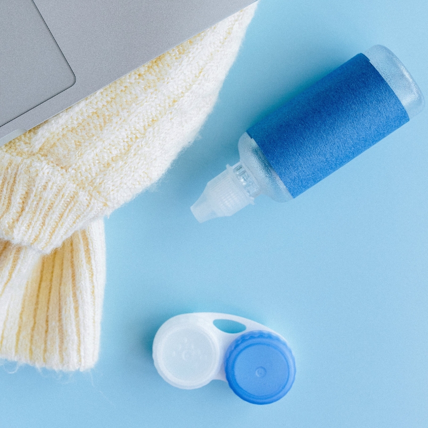 Contact lens solution bottle and lens case on a light blue surface.