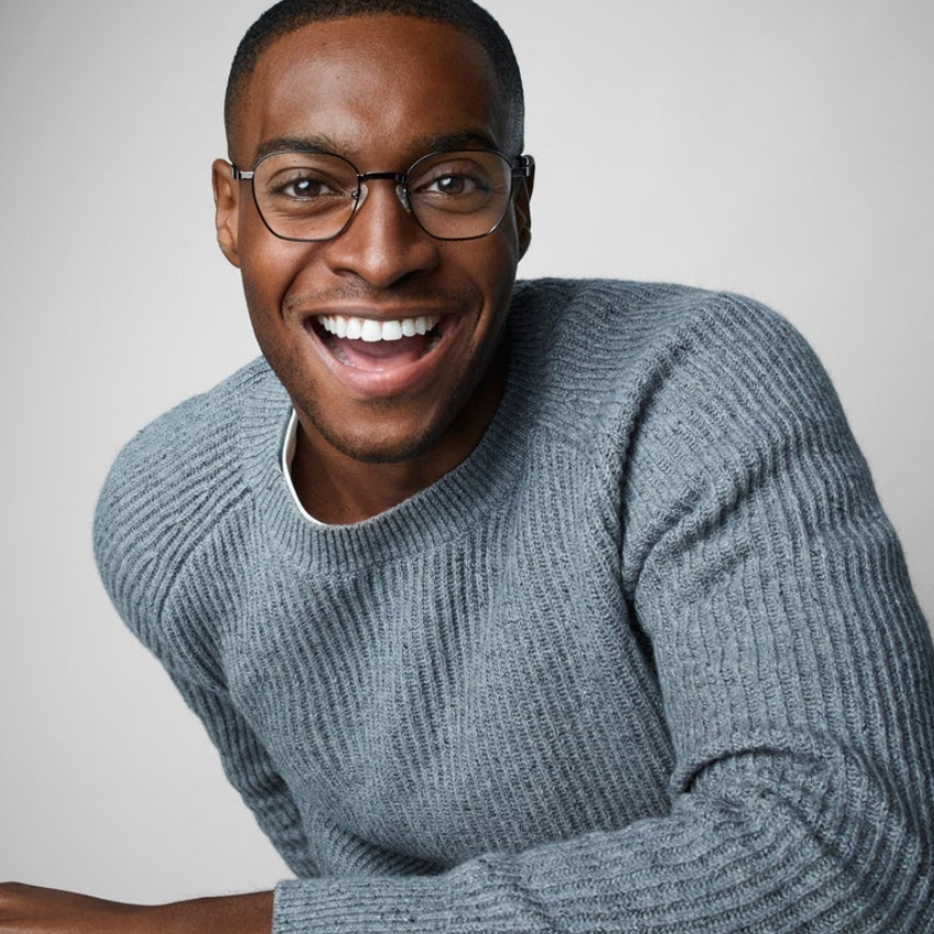 Man smiling, wearing round glasses and a grey knitted sweater.