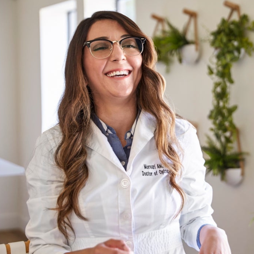 Female optometrist in a lab coat smiling; "Morvari Ahi, Doctor of Optometry" embroidered on the coat.