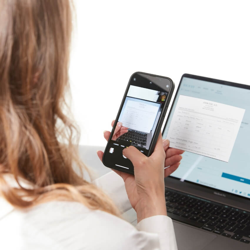 Person photographing a document with a smartphone in front of a laptop. Document text: Join SEC CLS.