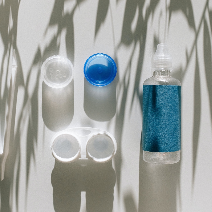 Contact lens solution bottle with blue label, lens case with blue and white caps, and lens case tweezers.