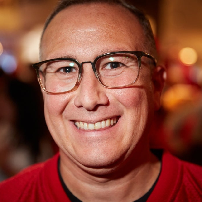 Man wearing glasses and a red shirt, smiling at the camera.