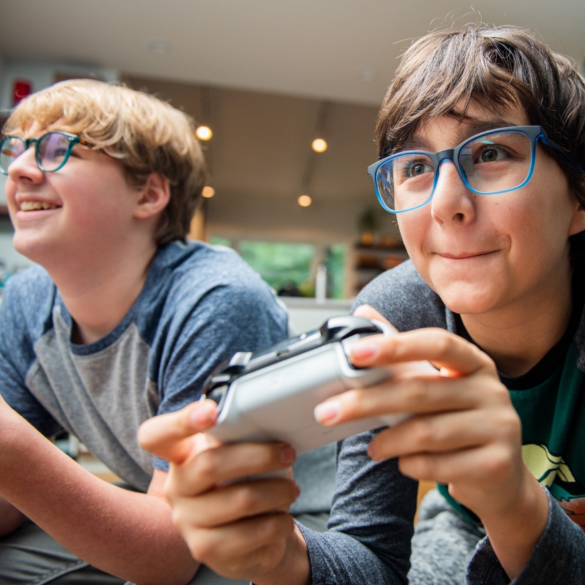 Two kids wearing glasses, playing video games, one holding a game controller with excitement.