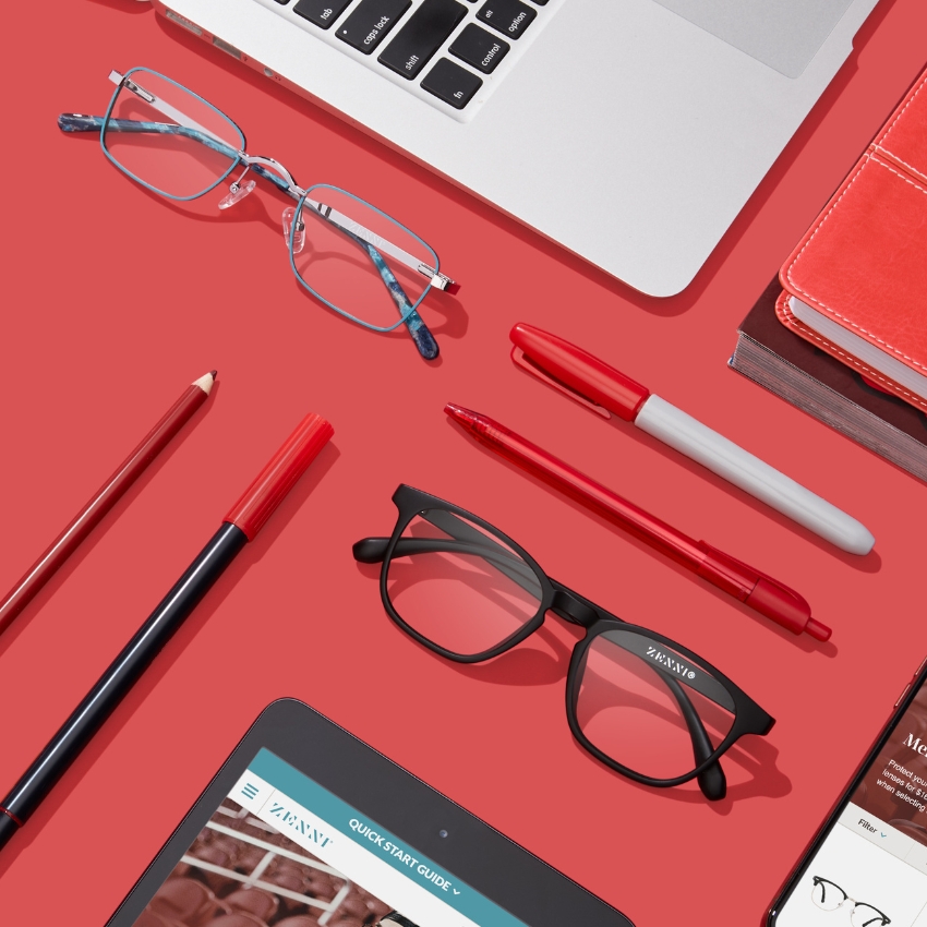 Eyeglasses by Zenni, one in blue frame and another in black frame, on a red background with pens and pencils.