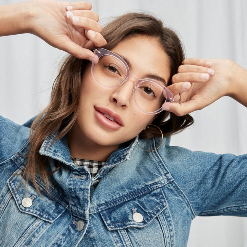 Woman wearing oversized clear-framed glasses and a blue denim jacket.