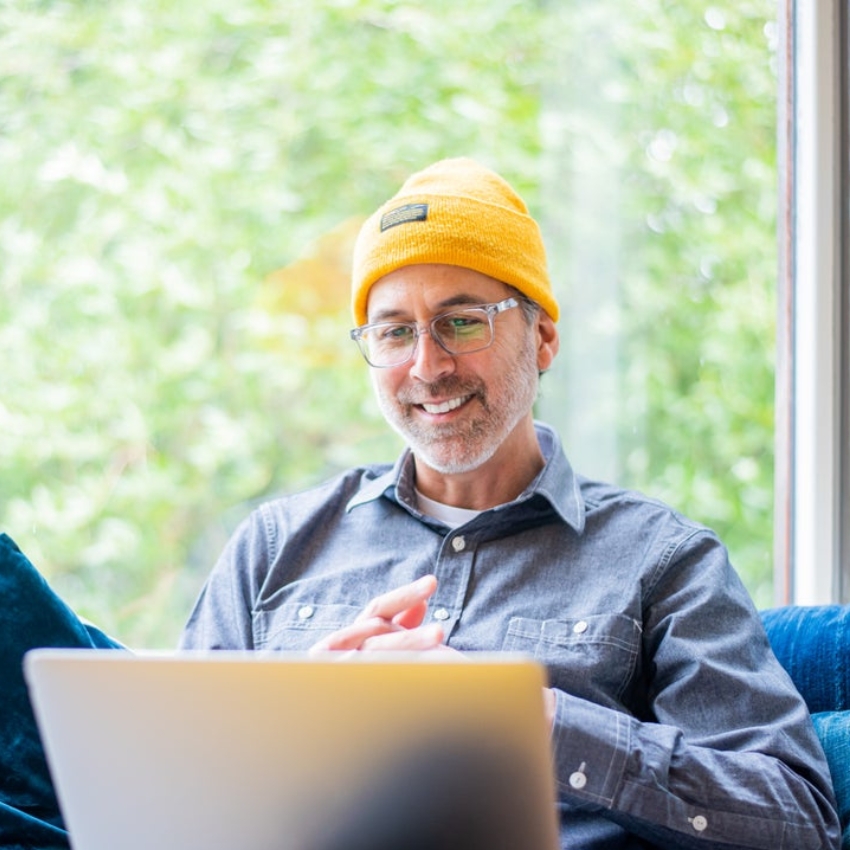 Man in a yellow beanie smiling while using a laptop.