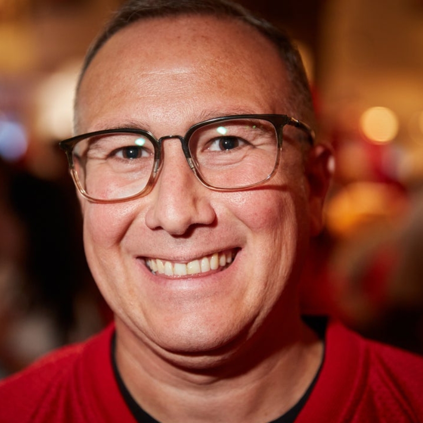 Man smiling, wearing glasses and a red top.