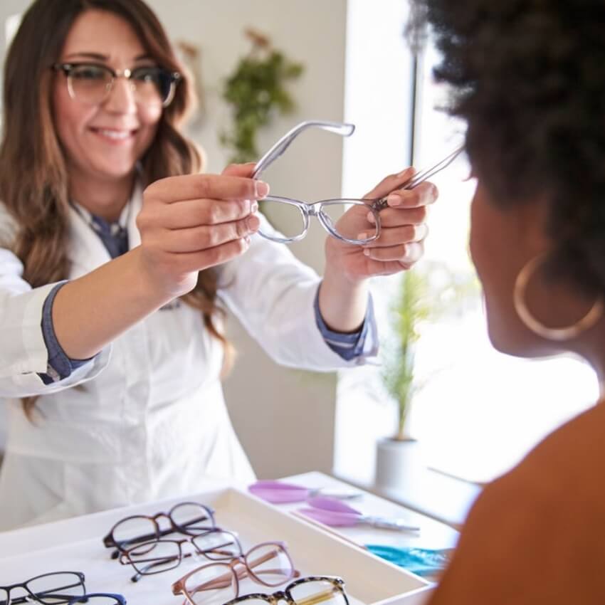 Optometrist presenting a pair of eyeglasses to a customer with multiple glasses displayed on the table.