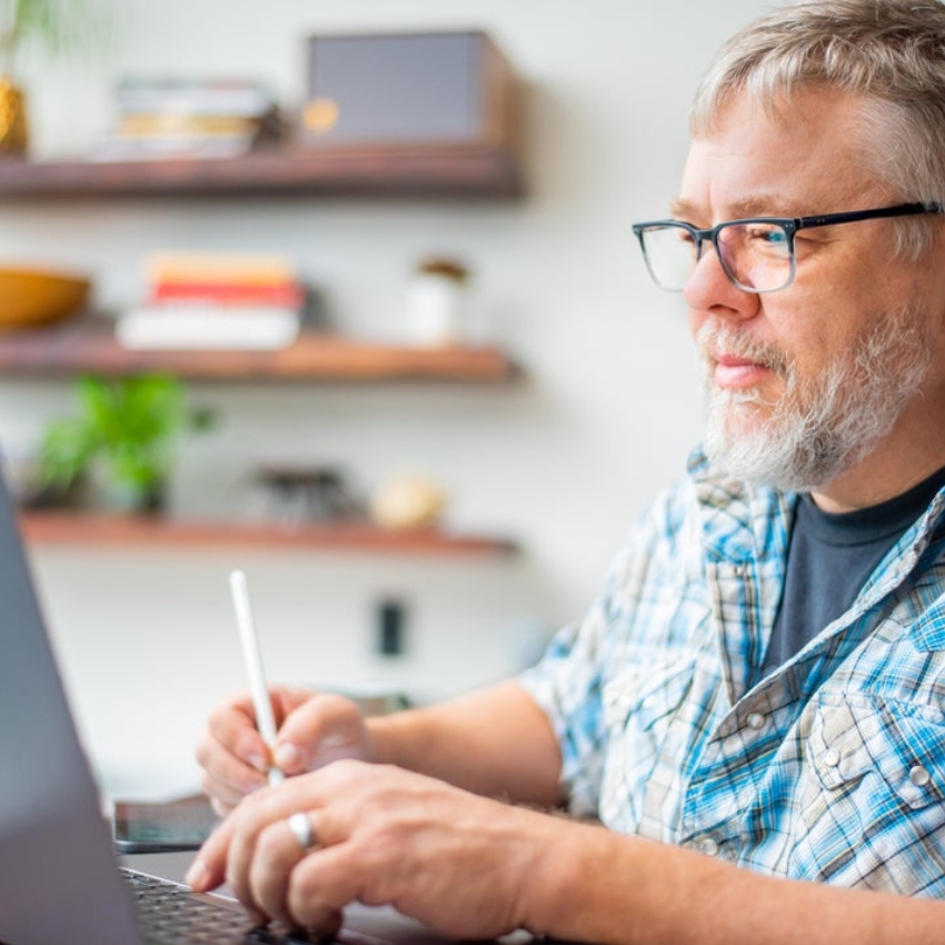 Man using a stylus and laptop in a home office.