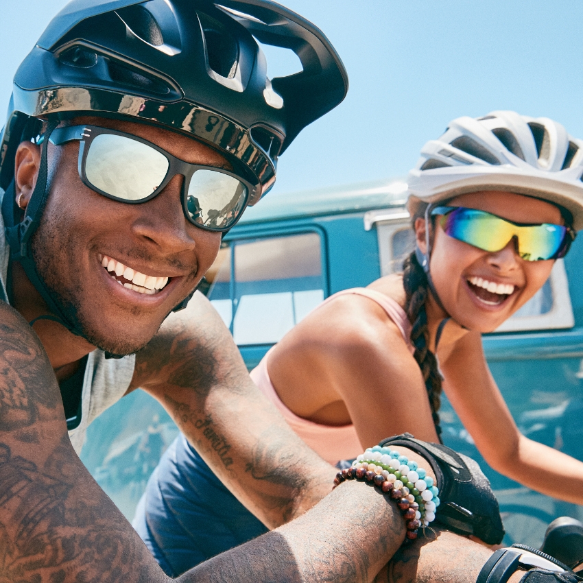 Smiling cyclists wearing helmets and reflective sunglasses.