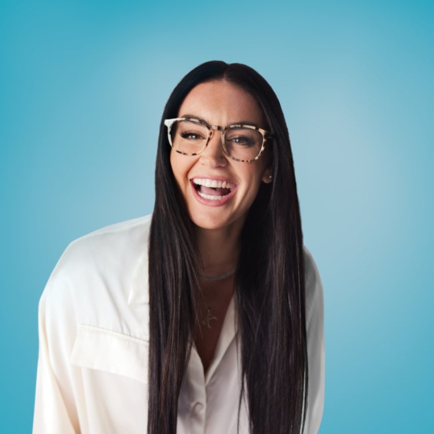 Woman with long dark hair wearing stylish oversized glasses and a white blouse, smiling broadly.