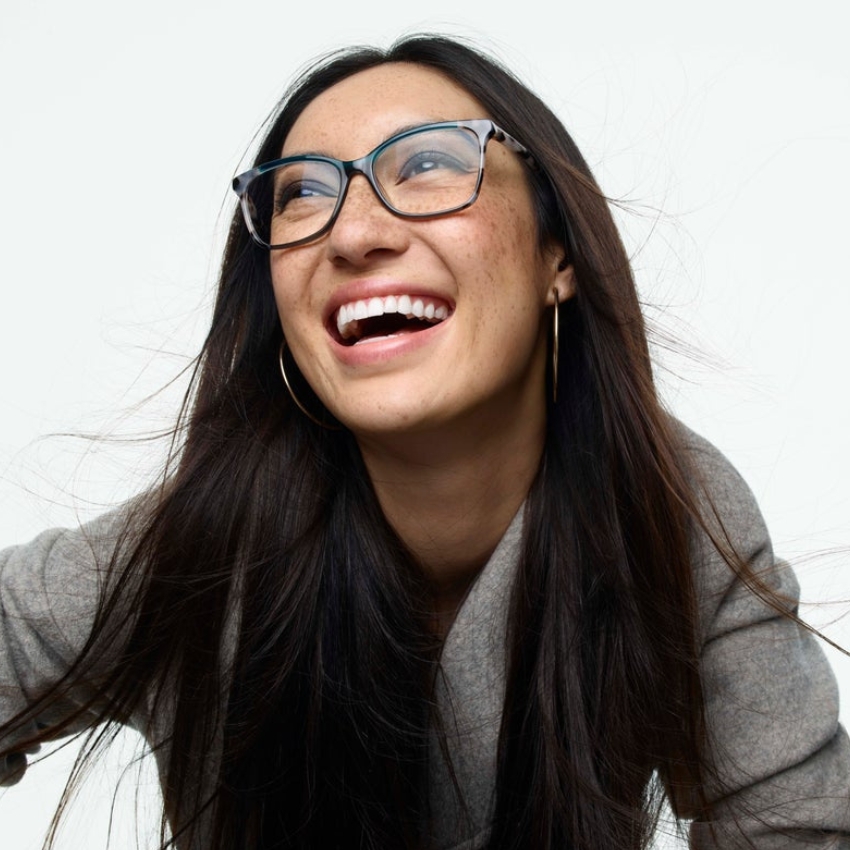 Woman wearing rectangular blue eyeglasses and large hoop earrings, smiling broadly.