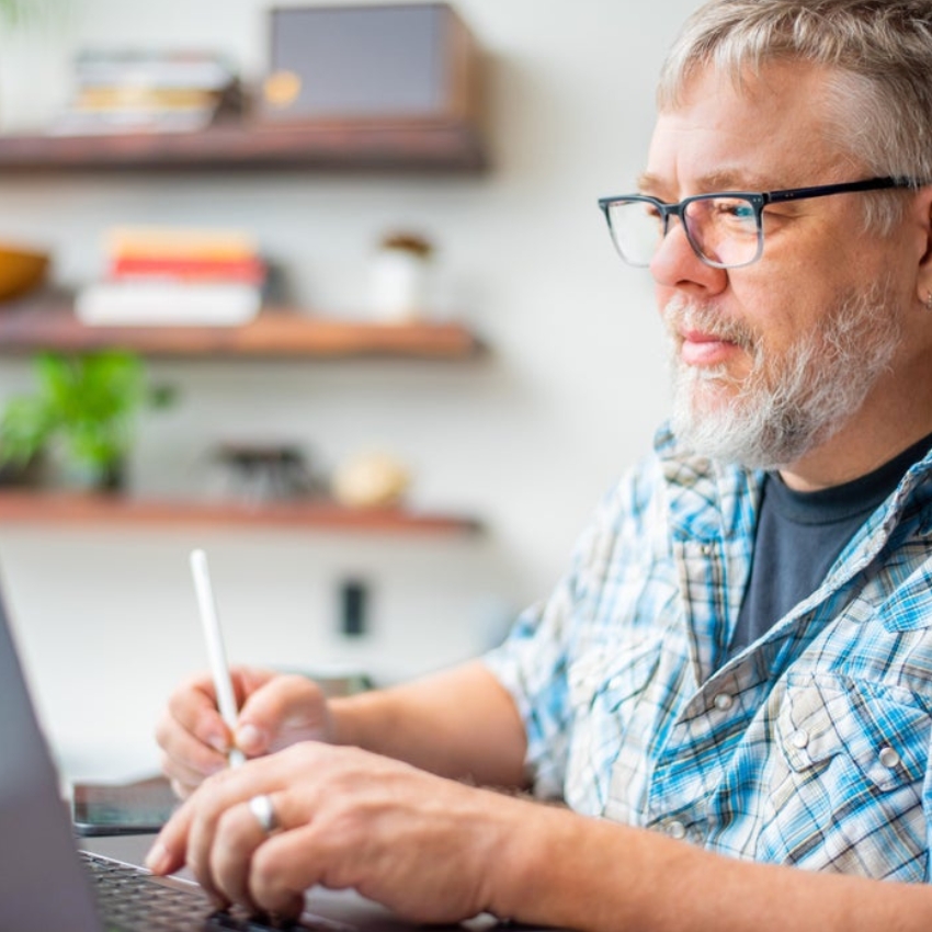 Man using a stylus on a tablet in front of a laptop.