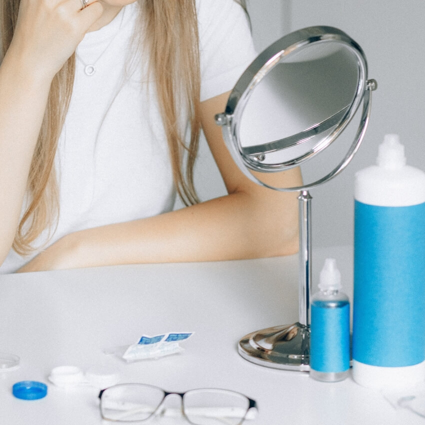 Contact lens care products, including a contact lens case, saline solution bottles, a small mirror, and glasses.