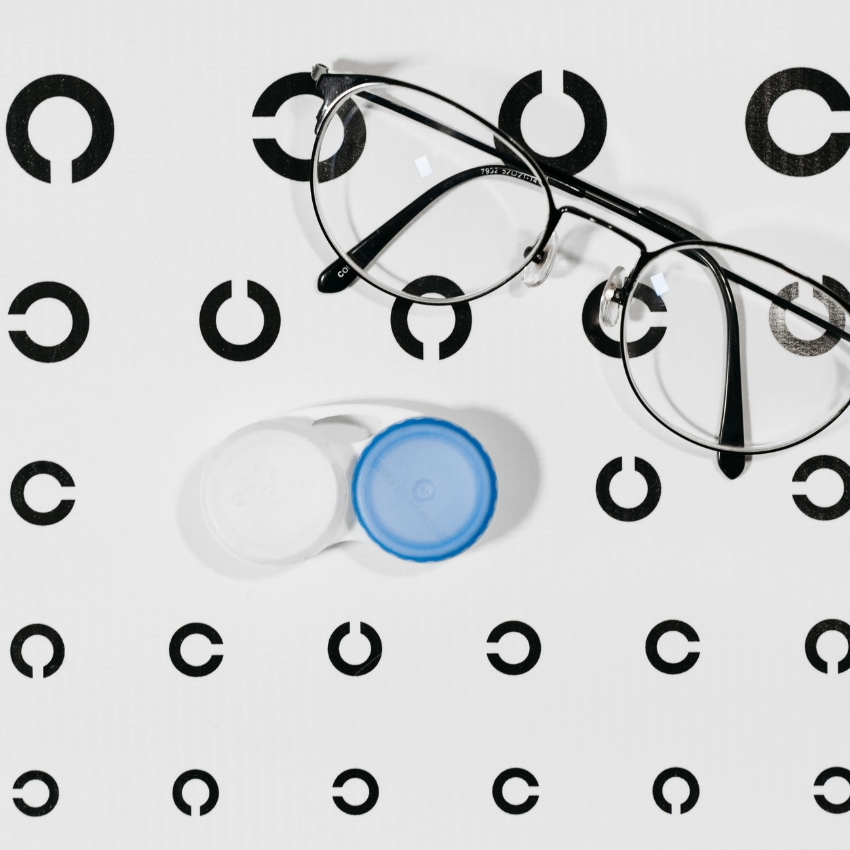 Eyeglasses with black frame and a contact lens case with one white and one blue cap.