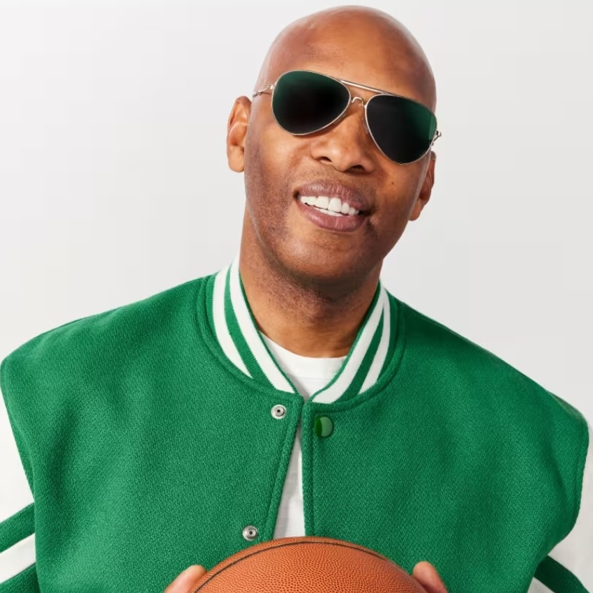 Man wearing a green varsity jacket and sunglasses, holding a basketball.