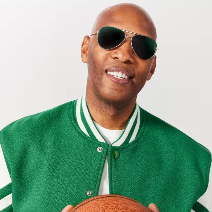 Man wearing sunglasses and a green varsity jacket, holding a basketball.