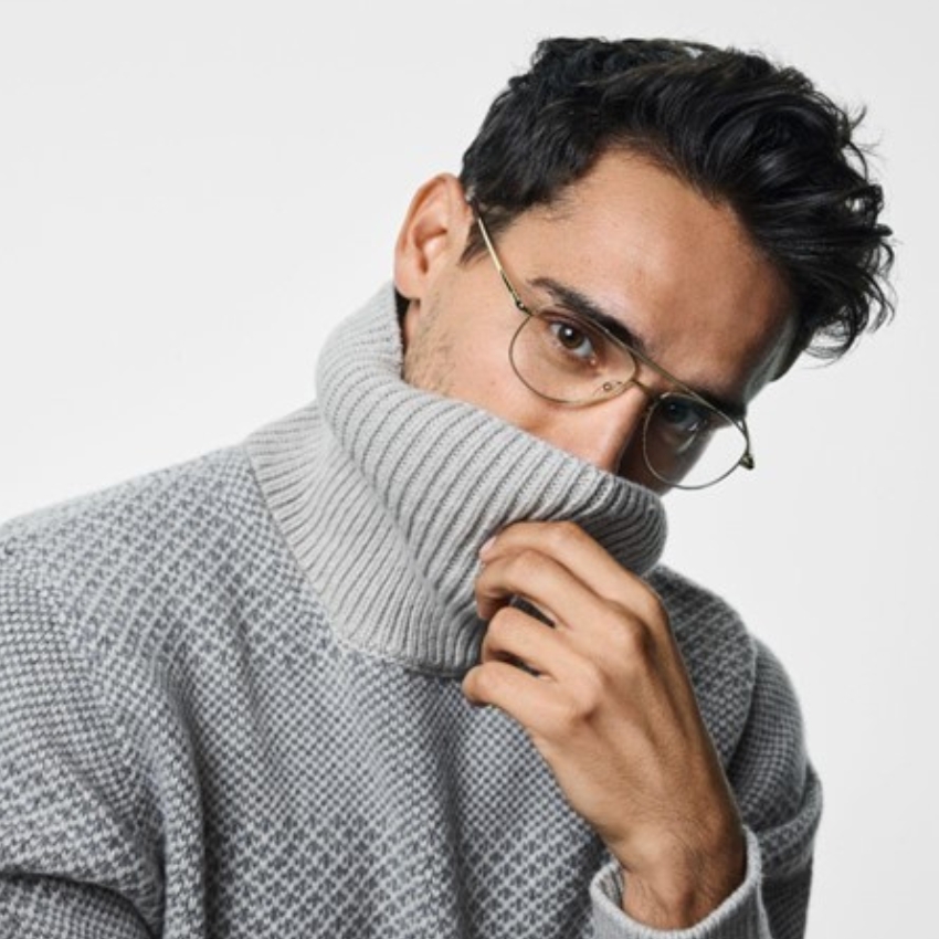 Man wearing a gray turtleneck sweater with a subtle geometric pattern and gold-rimmed glasses.