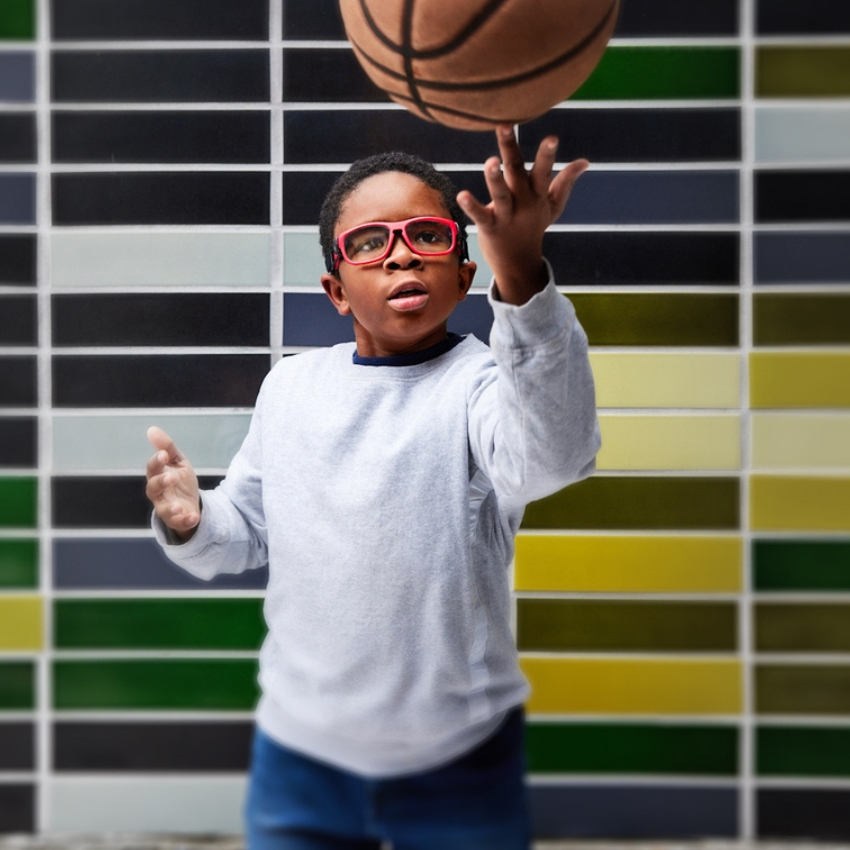 Child wearing red glasses and a grey sweater plays with a basketball.