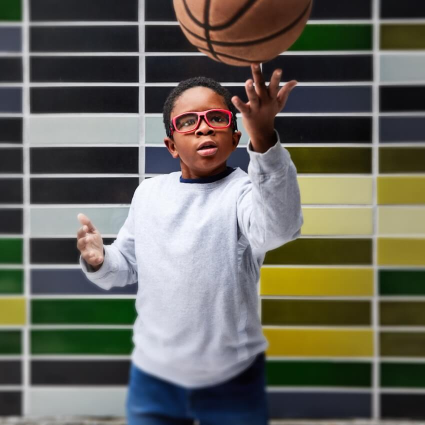 Boy wearing red glasses and a gray sweatshirt, spinning a basketball on his finger.