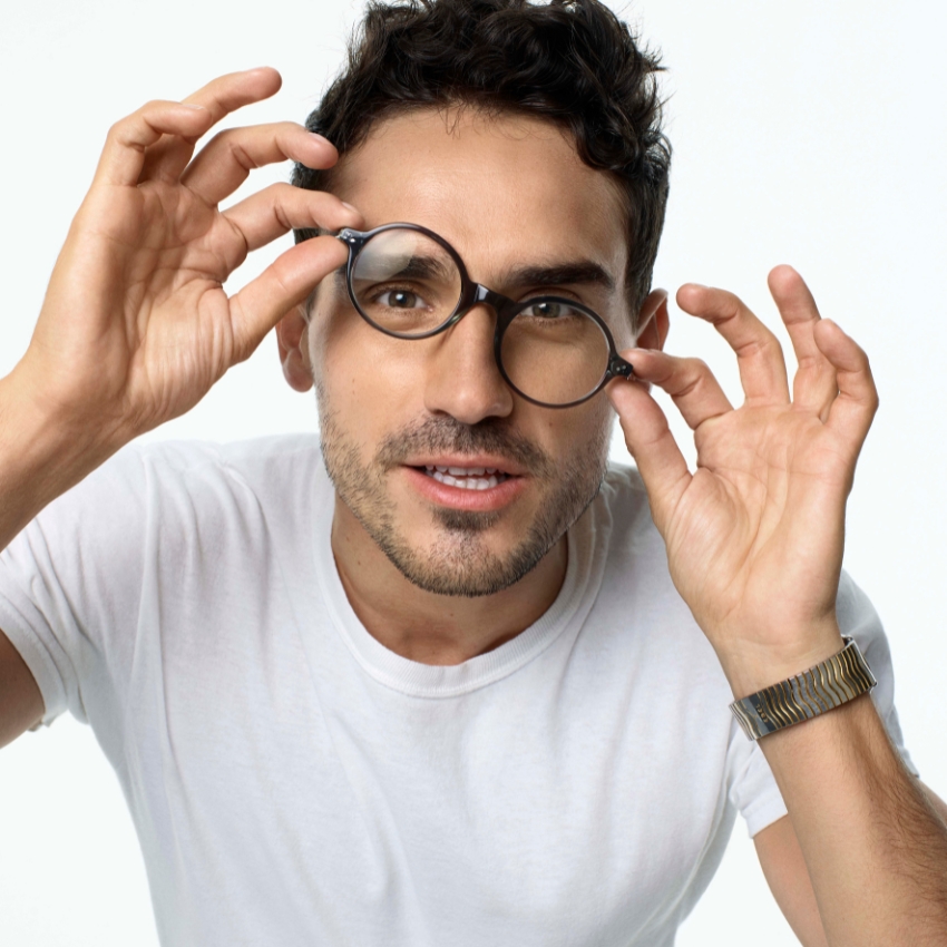 Man wearing round black glasses and white t-shirt, adjusting his glasses with both hands.