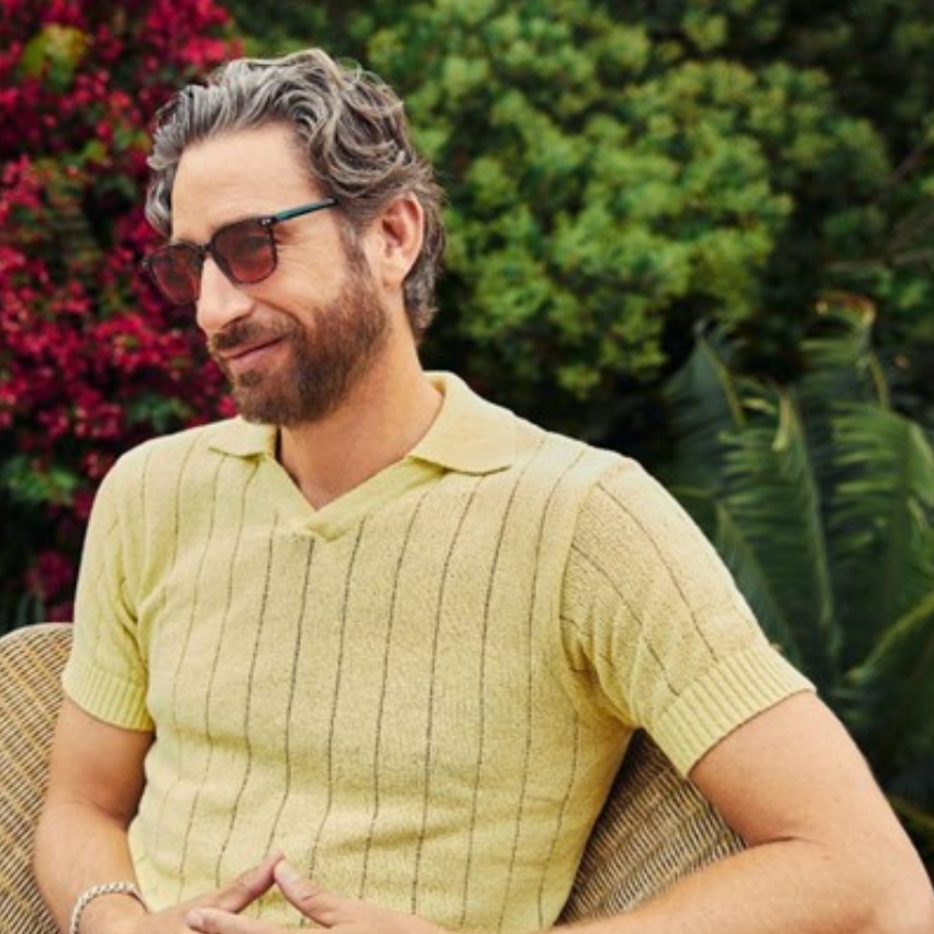 Man in a yellow knitted short-sleeve shirt with a collar and thin vertical stripes, wearing sunglasses.