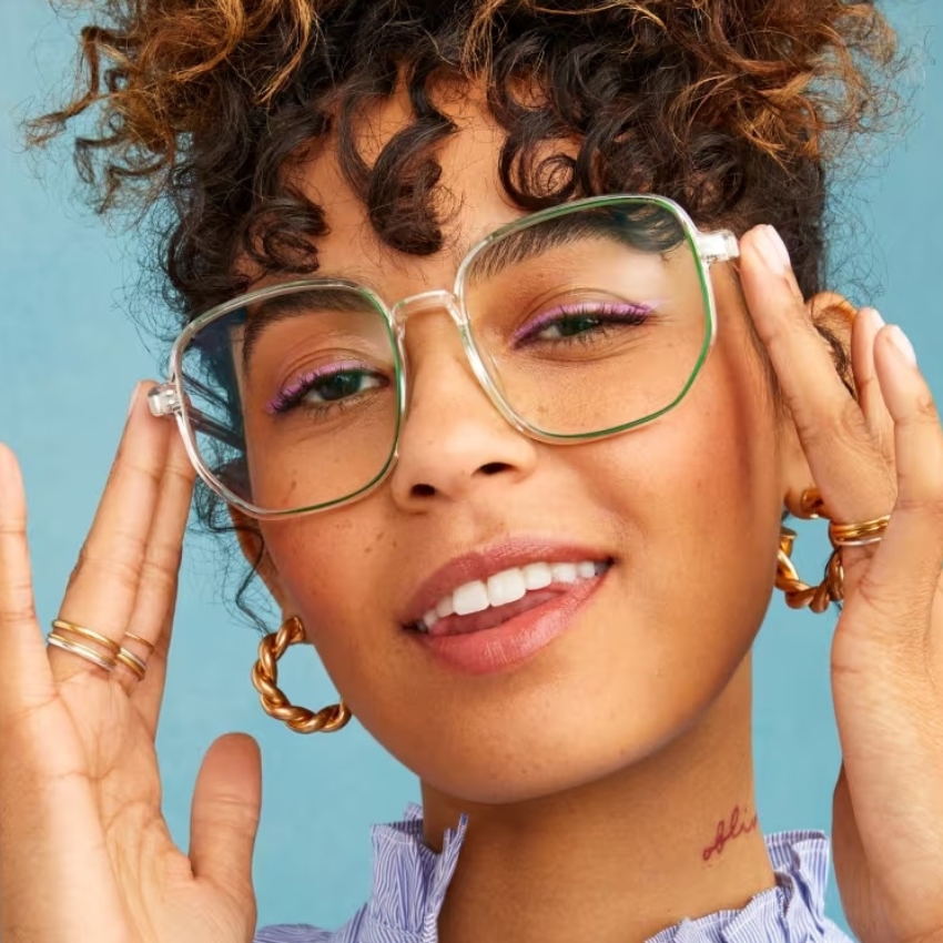 Transparent green-rimmed eyeglasses with bold geometric frames on a person adjusting them.