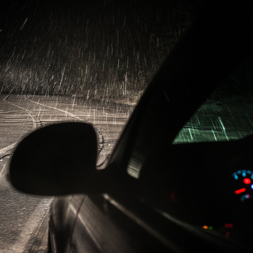 Car driving at night in heavy rain, with dashboard lights visible and headlights illuminating the wet road.