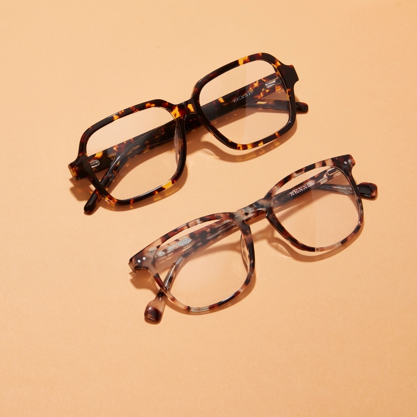 Two pairs of tortoiseshell eyeglasses on a beige surface.