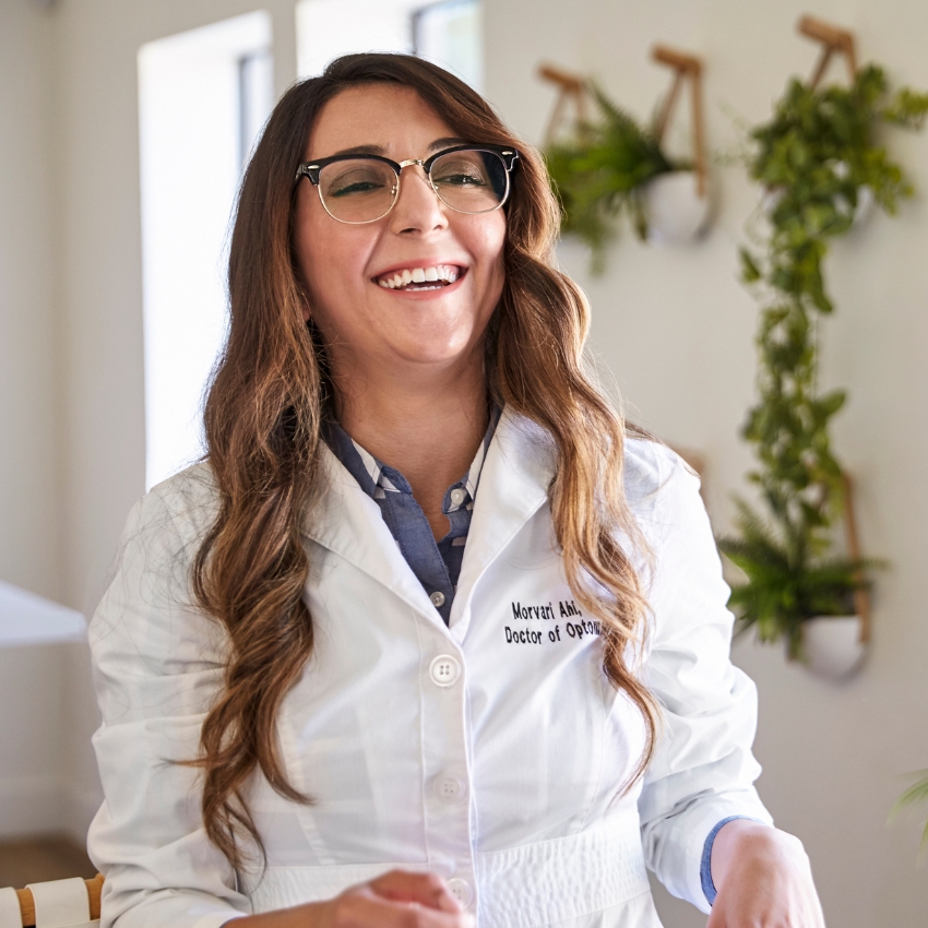 Smiling person wearing glasses and a white coat with text "Morvari Ahi, Doctor of Optometry".