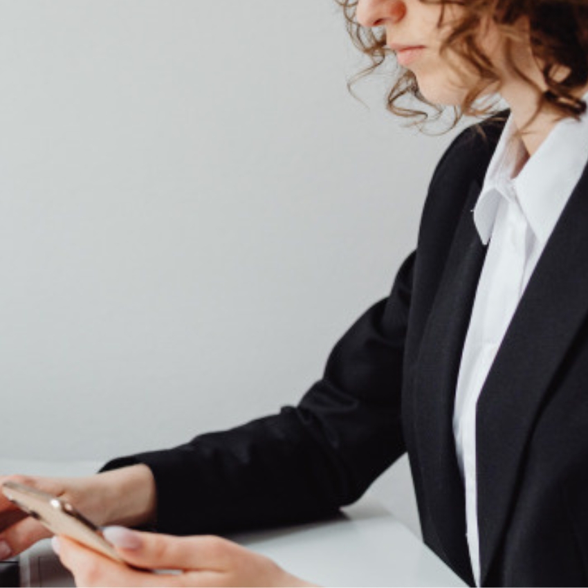 Person in black suit holding a smartphone, working on a laptop.